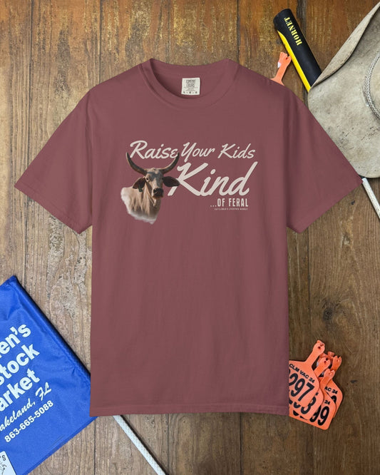 Maroon t-shirt with graphic and text on a wooden surface with accessories.