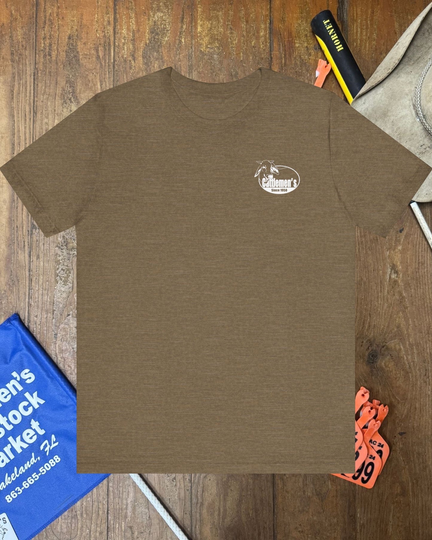 Brown t-shirt with a logo on a wooden surface with various items around