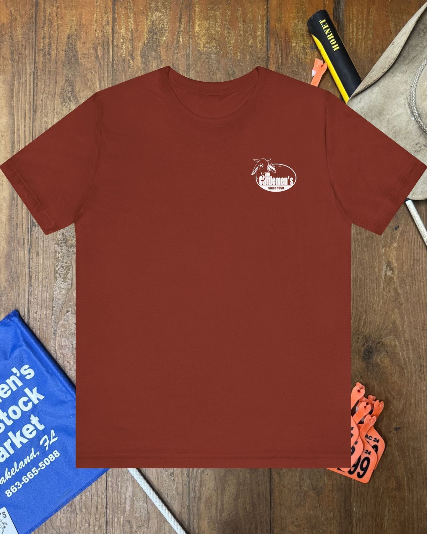 Brown t-shirt with a logo on a wooden surface with various items around