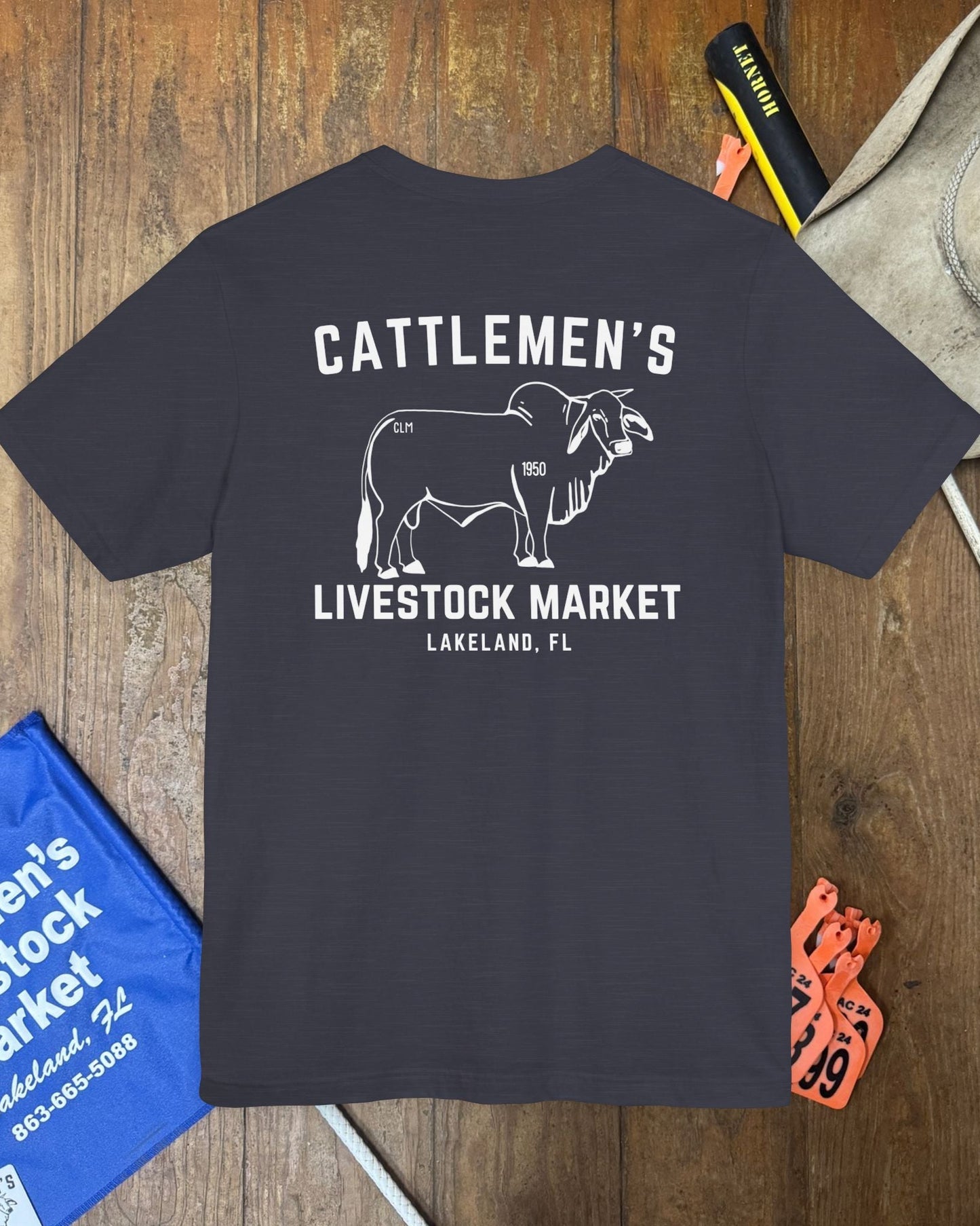 Navy blue t-shirt with 'Cattlemen's Livestock Market' text and bull graphic on a wooden surface.