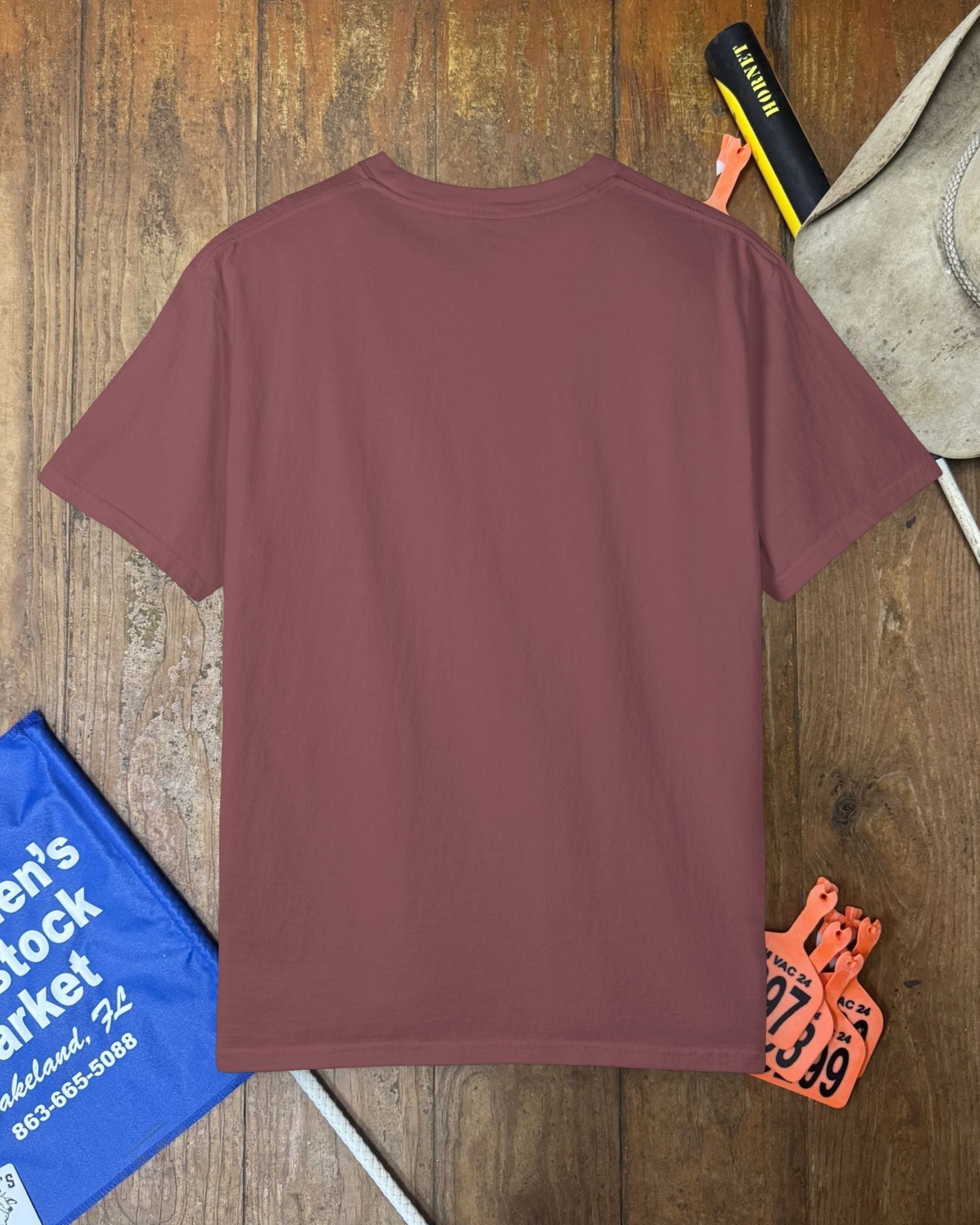 Maroon t-shirt on a wooden surface with various items around