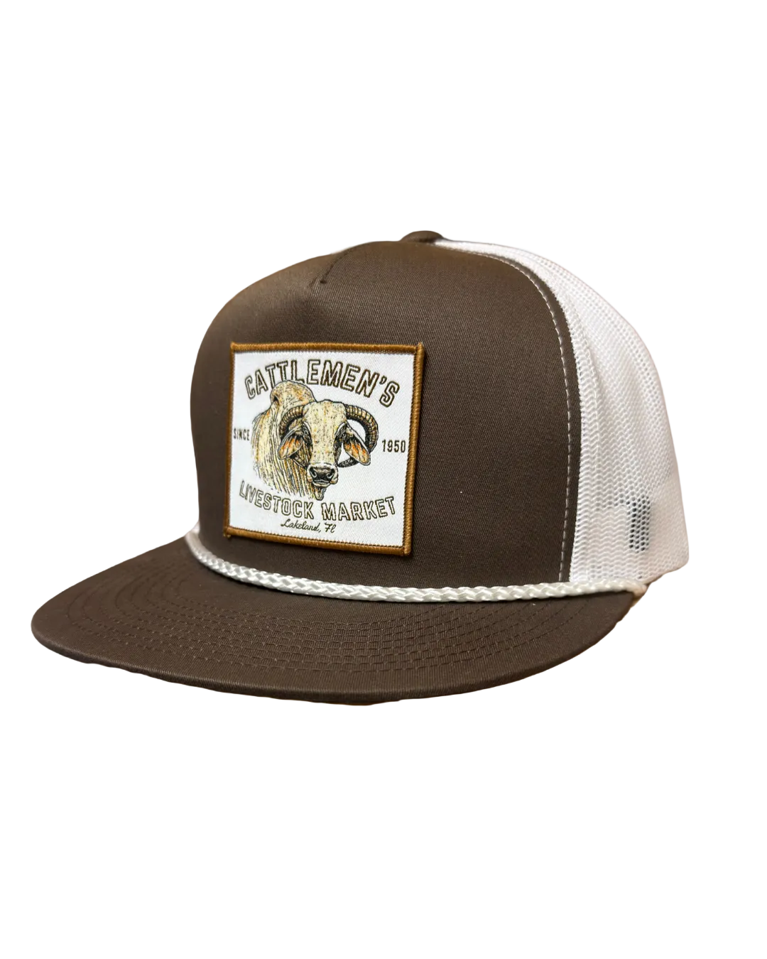 A brown and white trucker hat with a square embroidered patch on the front, resting on a wooden table in a rustic barn setting.