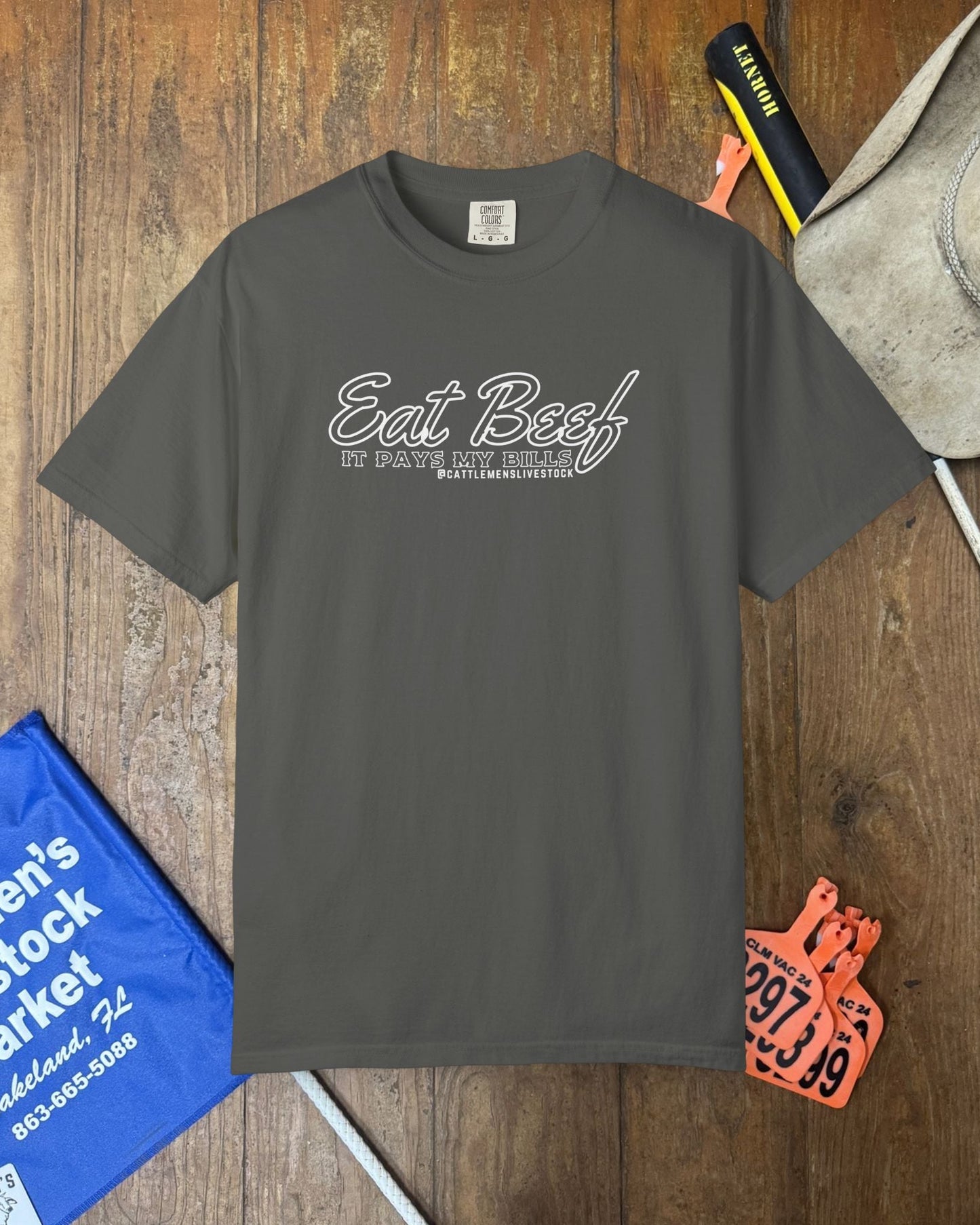 Gray t-shirt with 'Eat Beef' text on a wooden surface with various items around